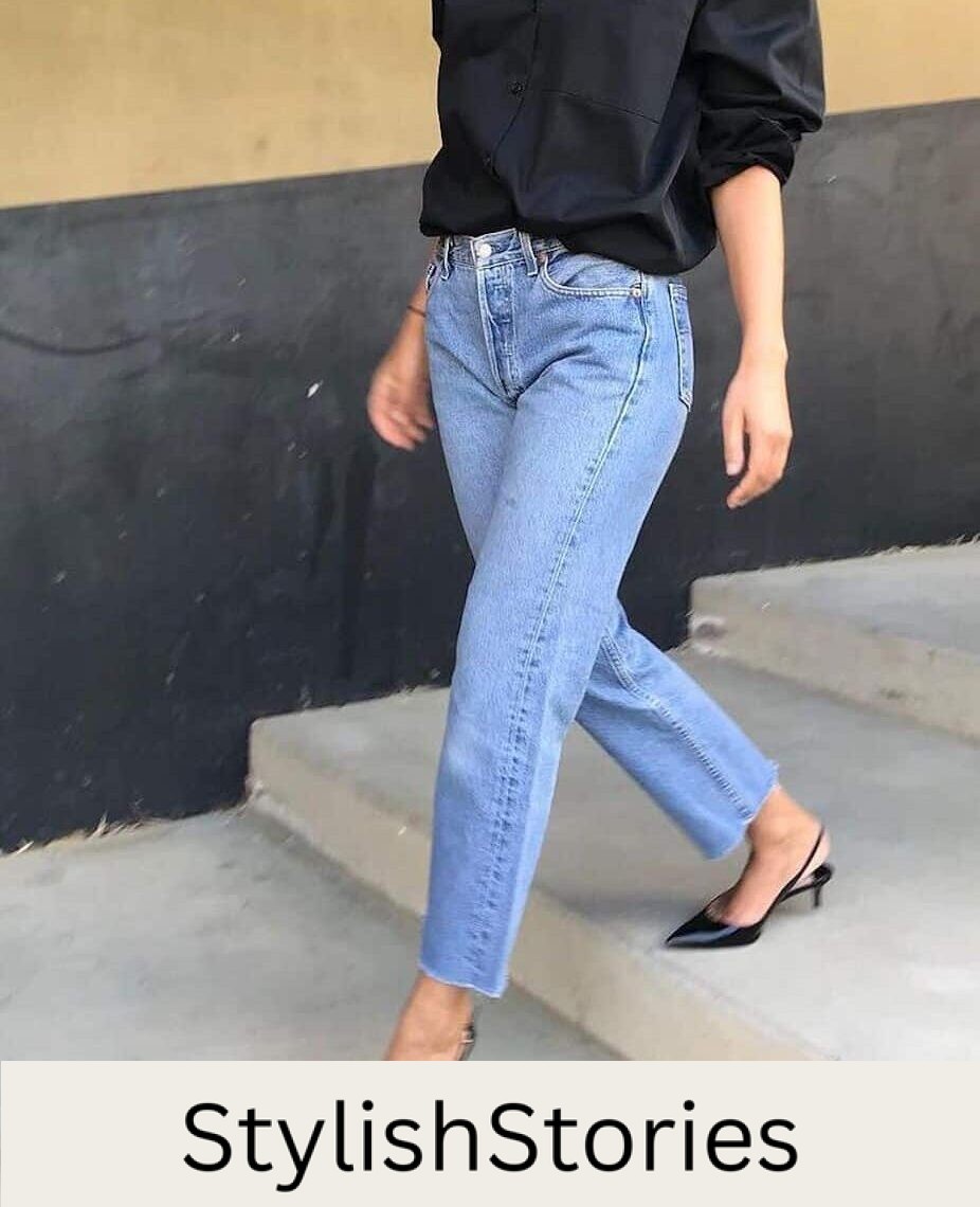 Woman wearing jeans, black kitten heels and a black button down blouse walks down concrete stairs.