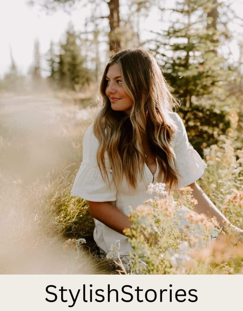 wholesome image of a teenage girl with brown hair wearing a white summer dress sitting on the ground among flowers posing for a senior photo