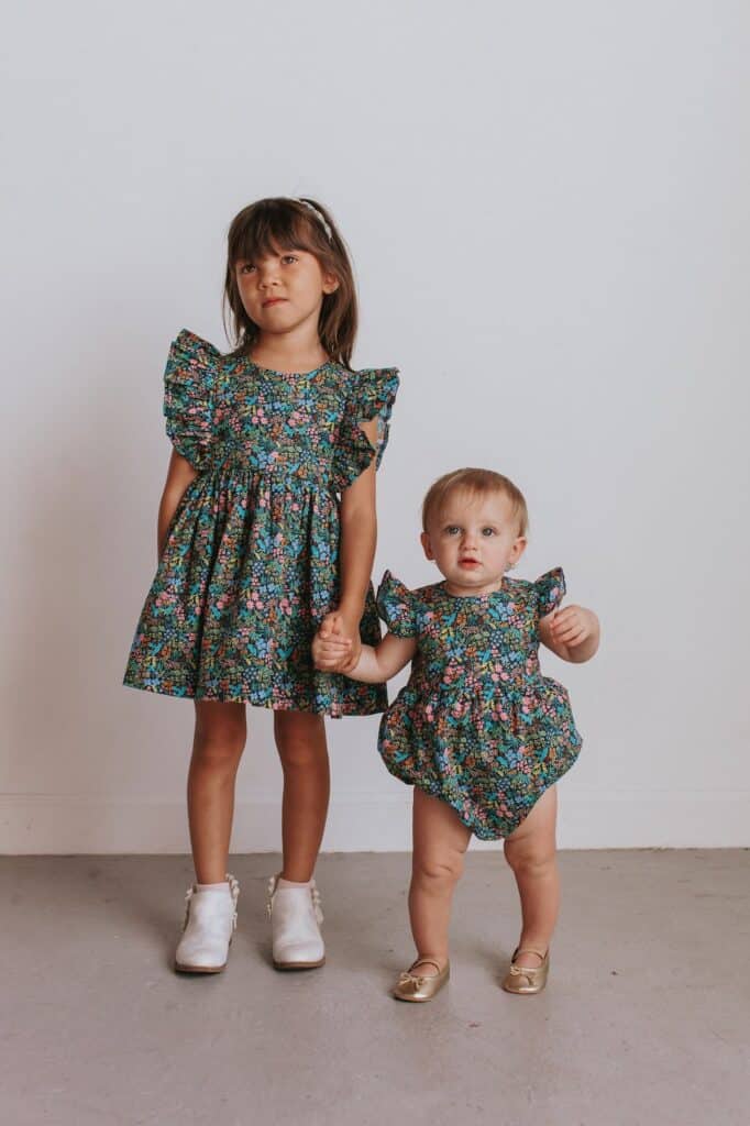 an image of a young girl and a small toddler wearing matching floral outfits holding hands