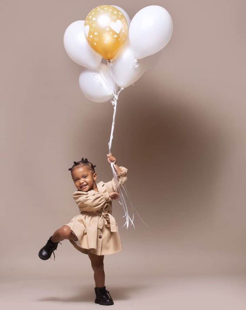 an image of a small girl against a neutral backdrop holding a bunch of balloons