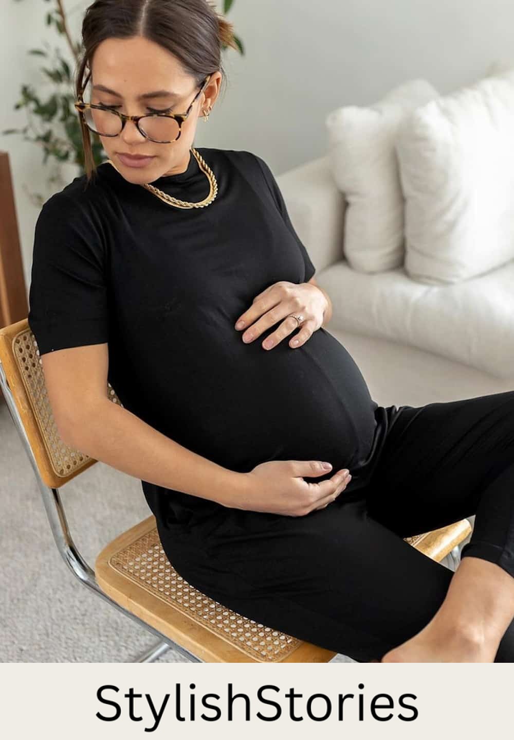 Pregnant woman sitting in a chair wearing a black short-sleeved jumpsuit romper