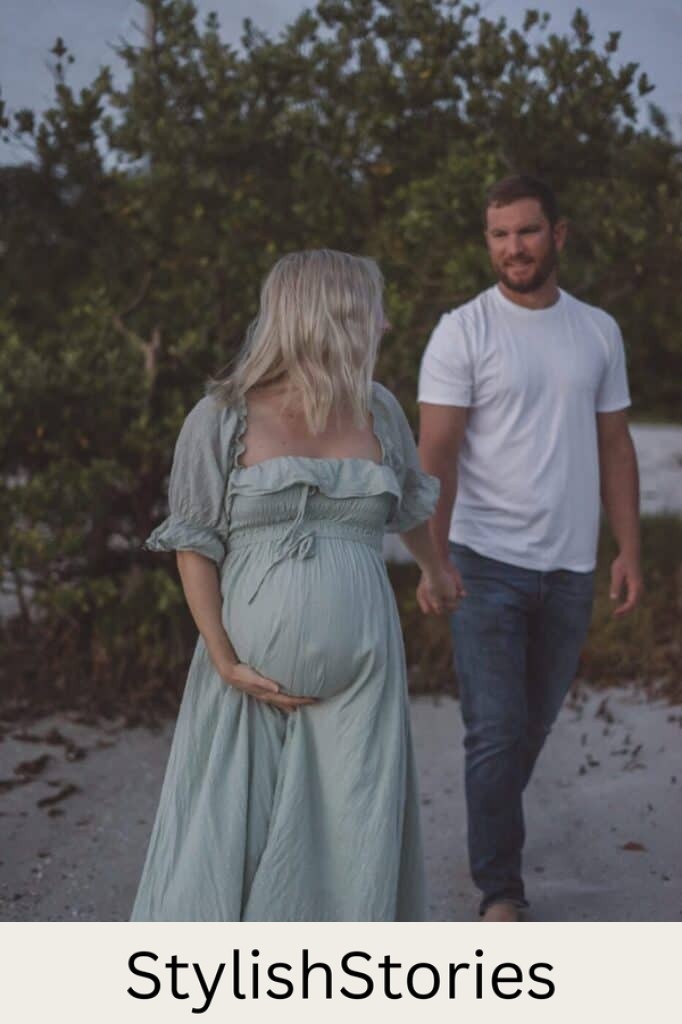 image of a pregnant woman leading a man onto a beach, she is wearing a long light green flowing dress and he is in a white t-shirt with jeans