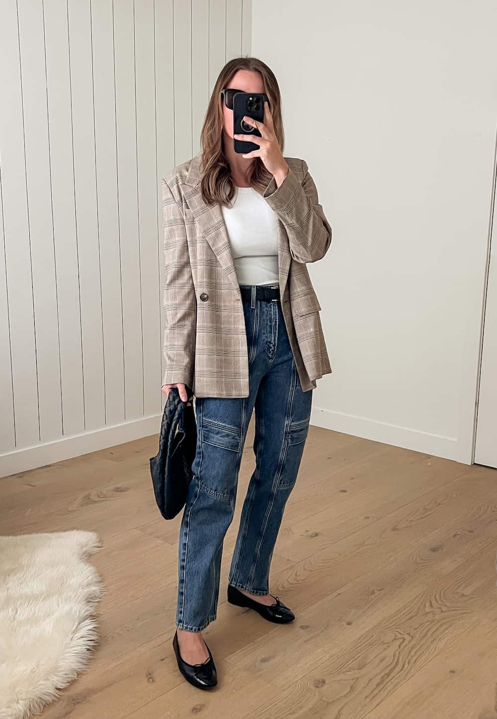 Woman wearing utility jeans and a white tank top with a plaid blazer and ballet flats.