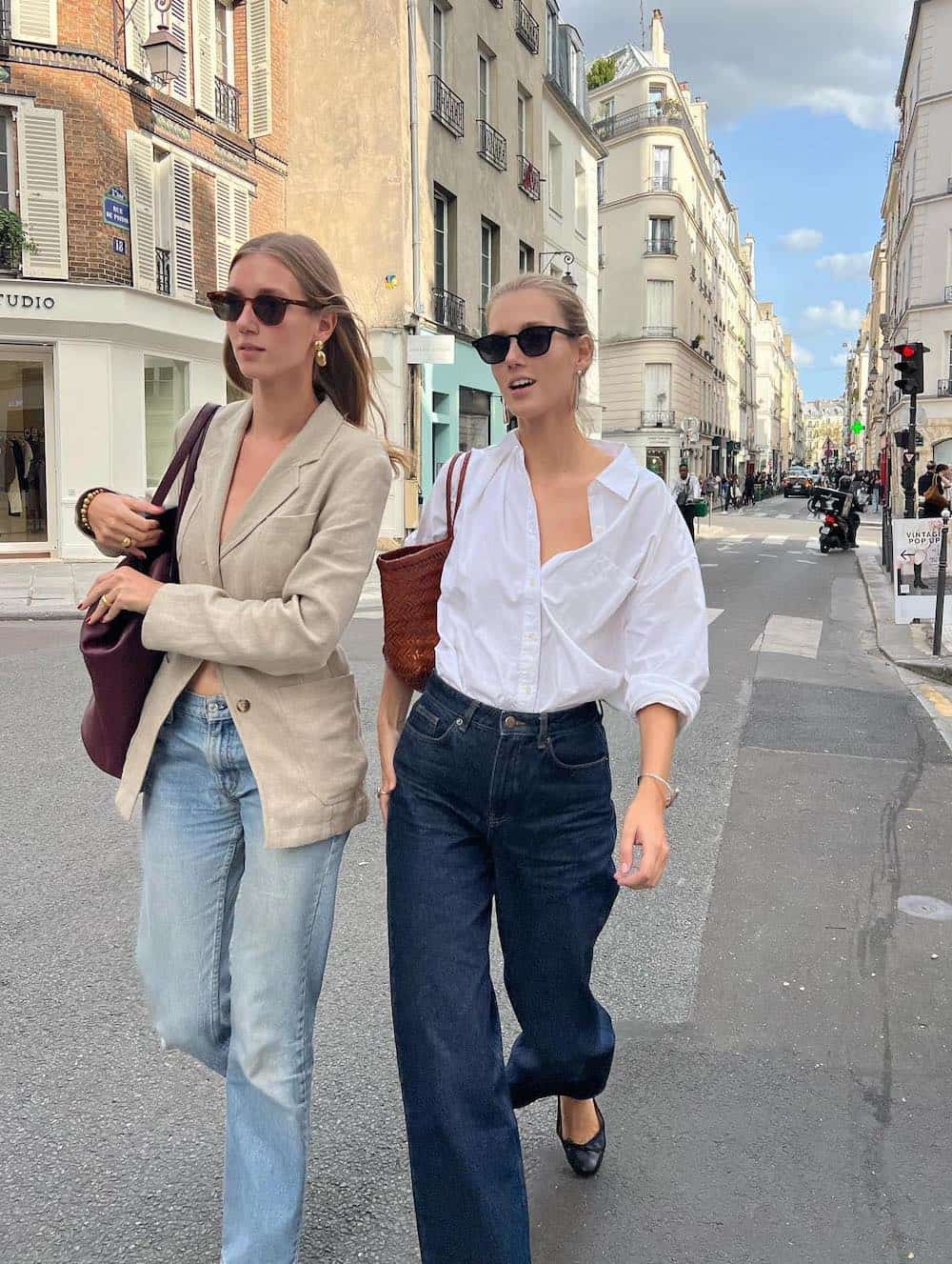 Two women walking down the street wearing jeans and button downs.