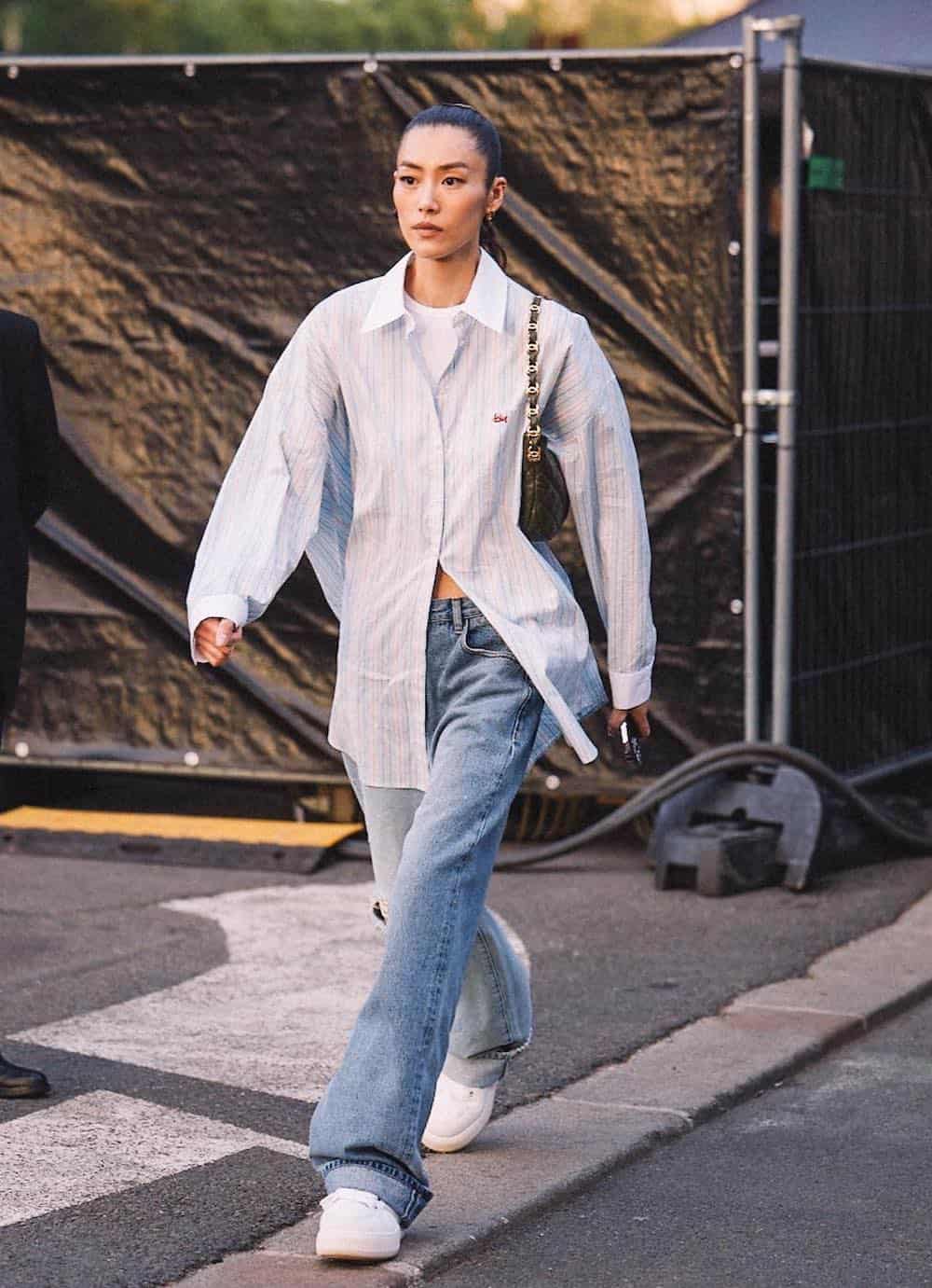 Woman wearing jeans, white sneakers, a white cropped top and an oversized button down.