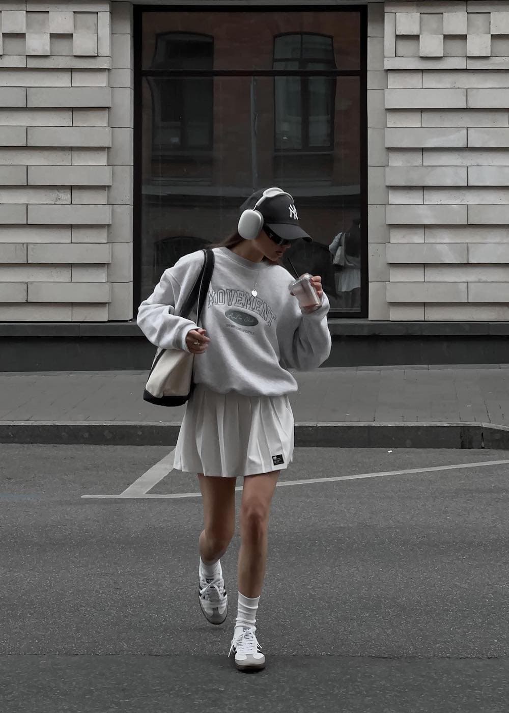 a woman wearing a soft grey sweatshirt with a white tennis skirt and sneakers