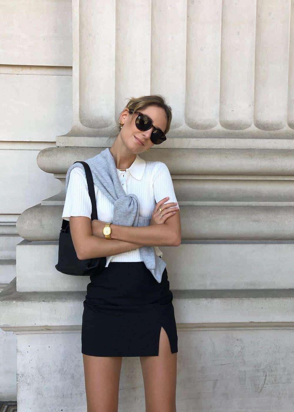 a woman wearing a black slitted mini skirt with a ribbed white tee and a grey sweater tied over her shoulders