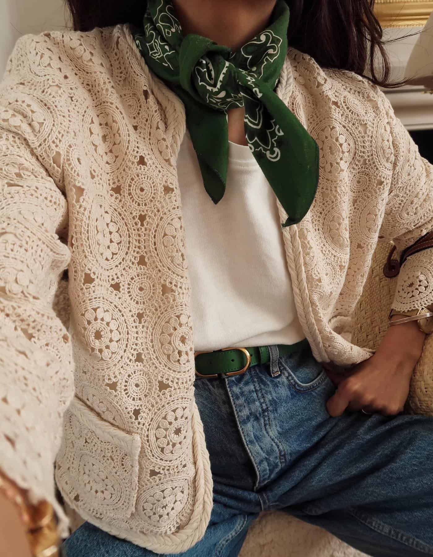 Woman wearing jeans with a white tee and a crochet jacket with a green belt and green bandana.