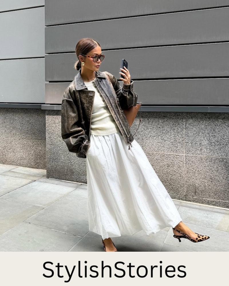 Woman wearing a white bubble hem skirt with a white tank and a brown leather jacket.