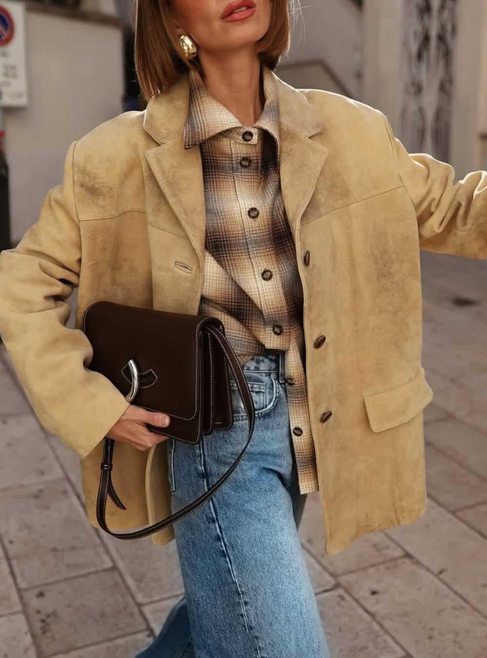Woman wearing jeans with a plaid button down and a suede coat.