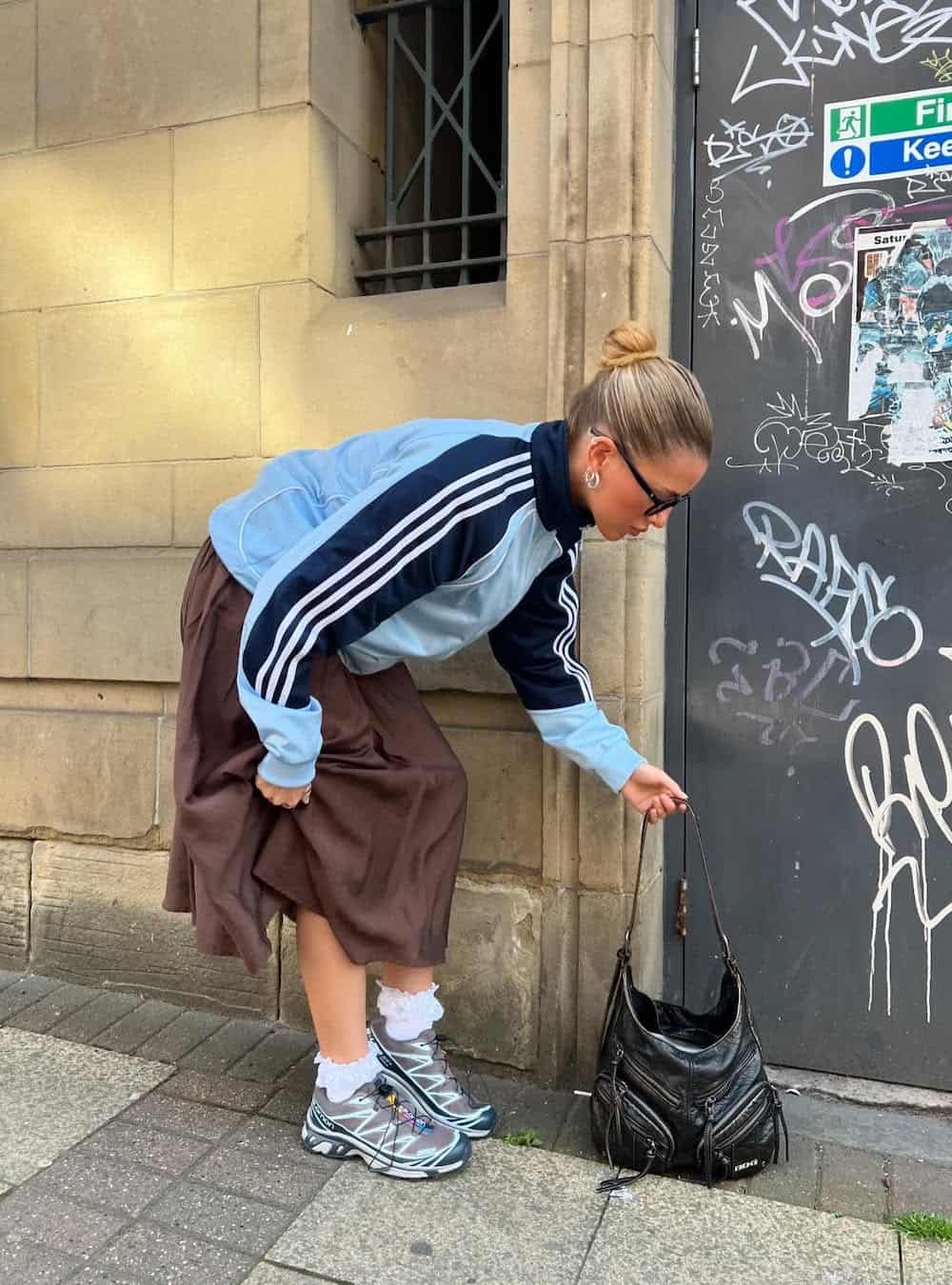 Woman wearing a satin skirt with sneakers and a blue sweater.