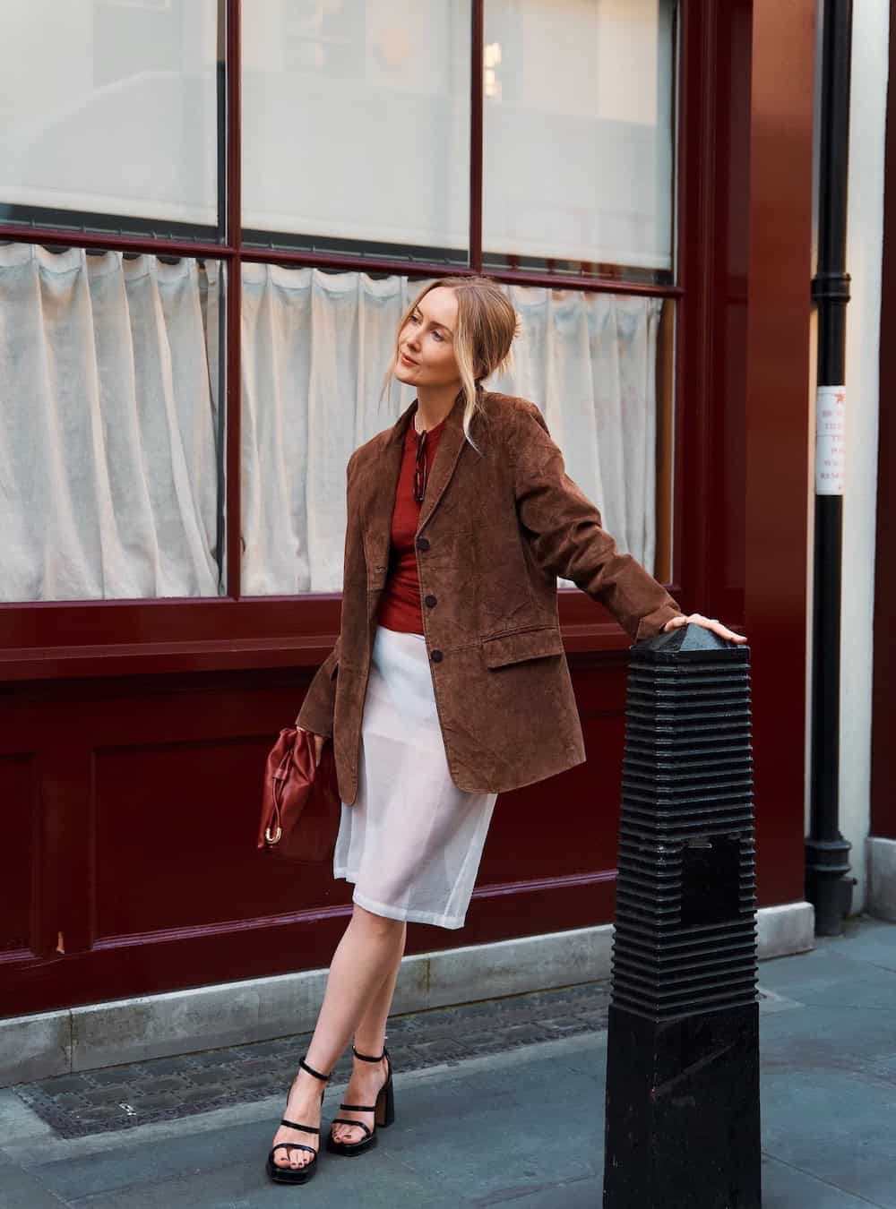Woman wearing a white skirt with an oversized brown blazer and heels.