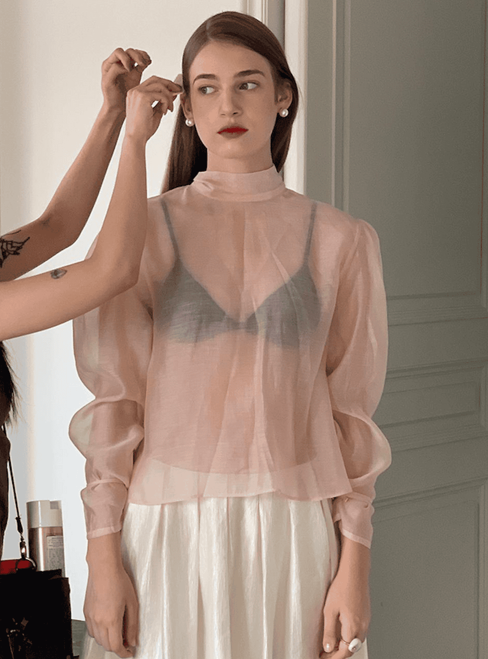 Woman wearing a black bralette with a see through blouse and a satin skirt.