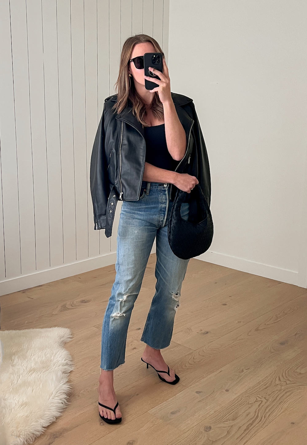 Woman wearing distressed jeans, a black tank top and a black leather jacket with heels.