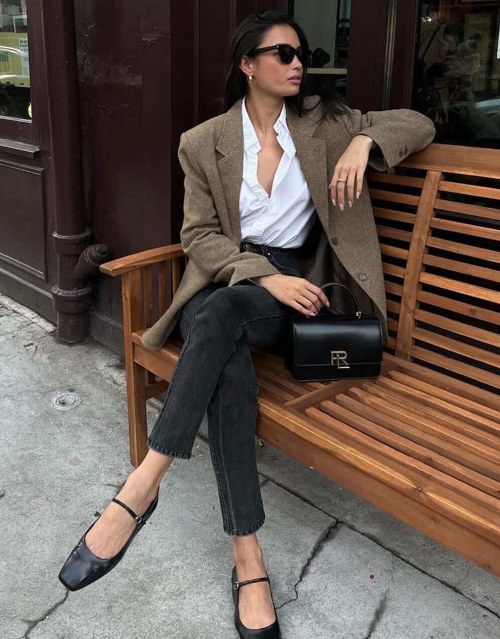 Woman wearing black skinny jeans, black ballet flats, a white button down and a brown blazer.