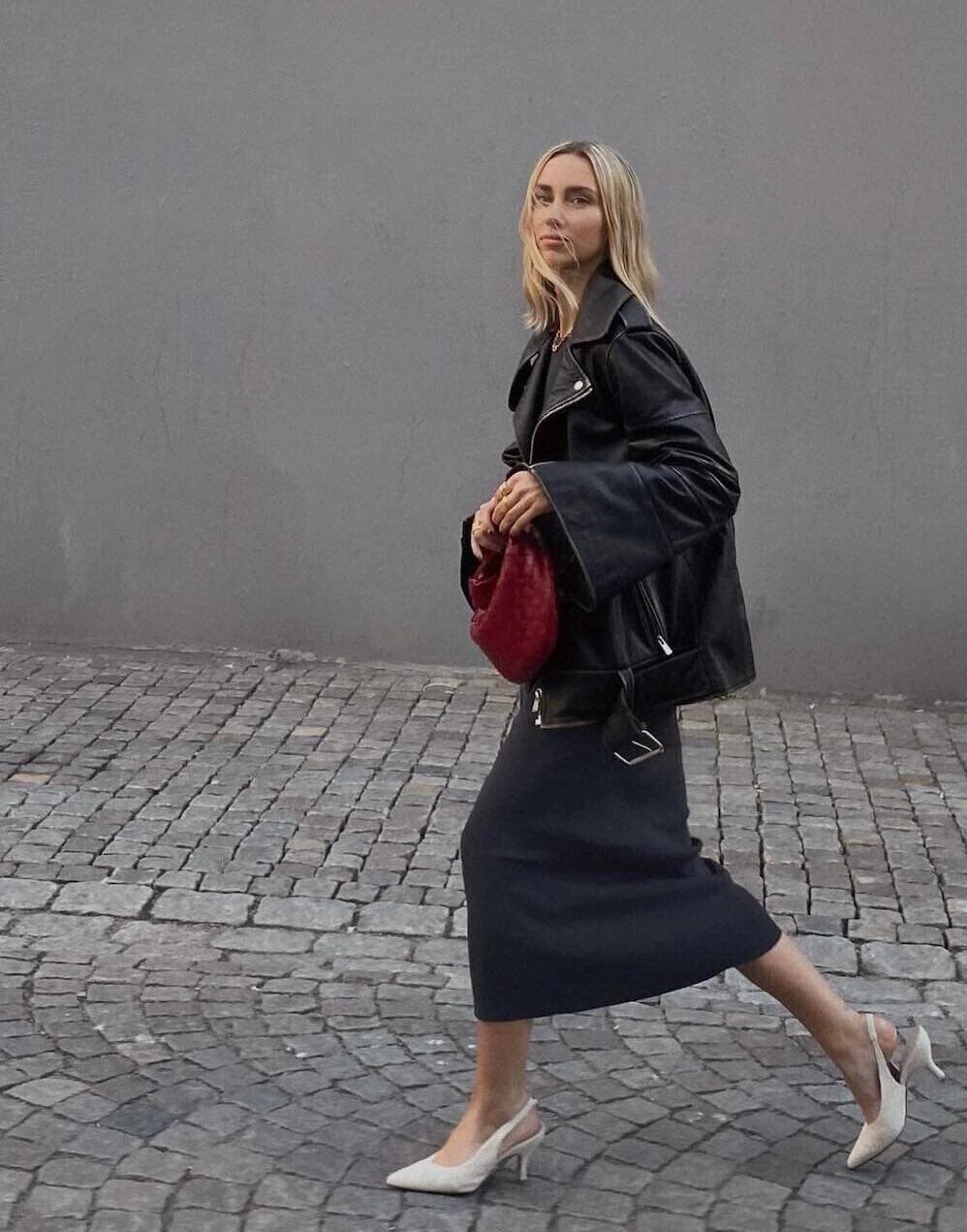 Woman wearing a black slip skirt with sling back pumps and a black leather jacket.