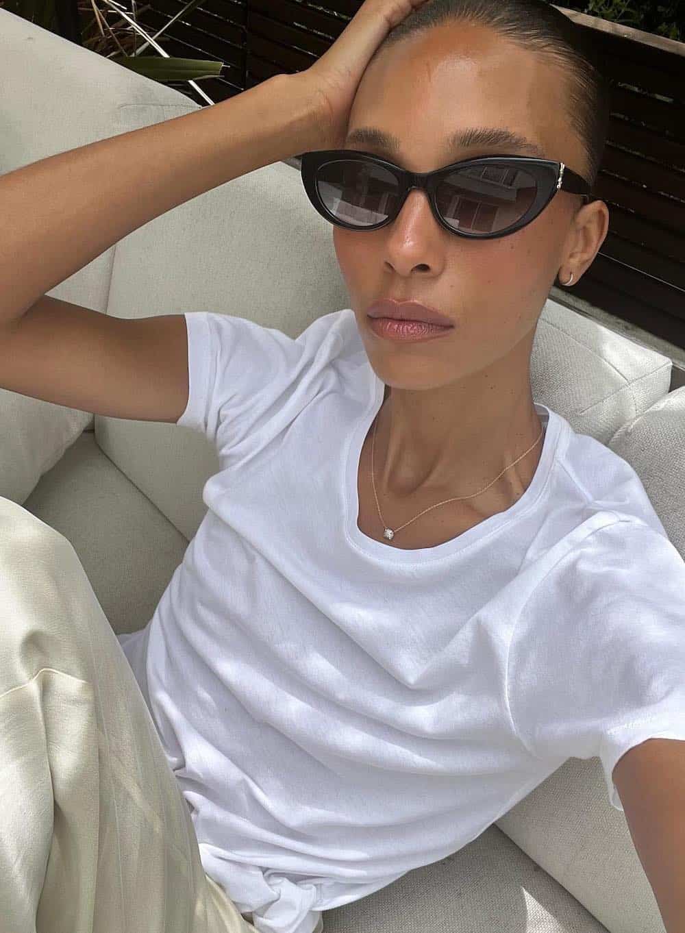 Off-duty model Tylynn Nguyen wearing cream colored trousers and a white t-shirt with black sunglasses and simple jewelry.