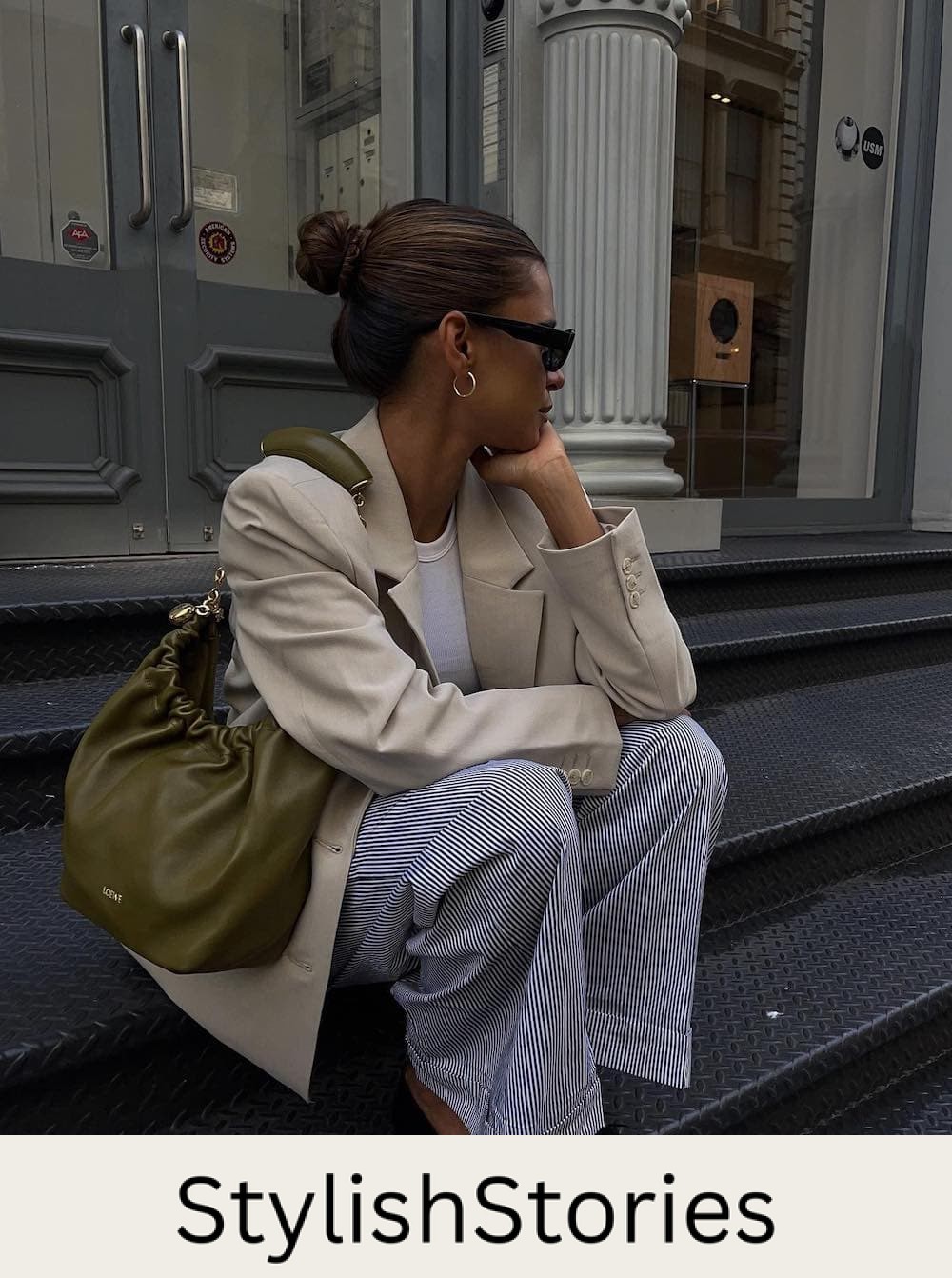 Woman wearing blue and white striped trousers with black ballet flats a white t-shirt and a tan blazer.