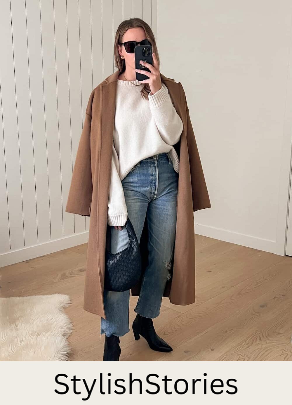Woman wearing jeans, black boots a white sweater and a brown trench coat.