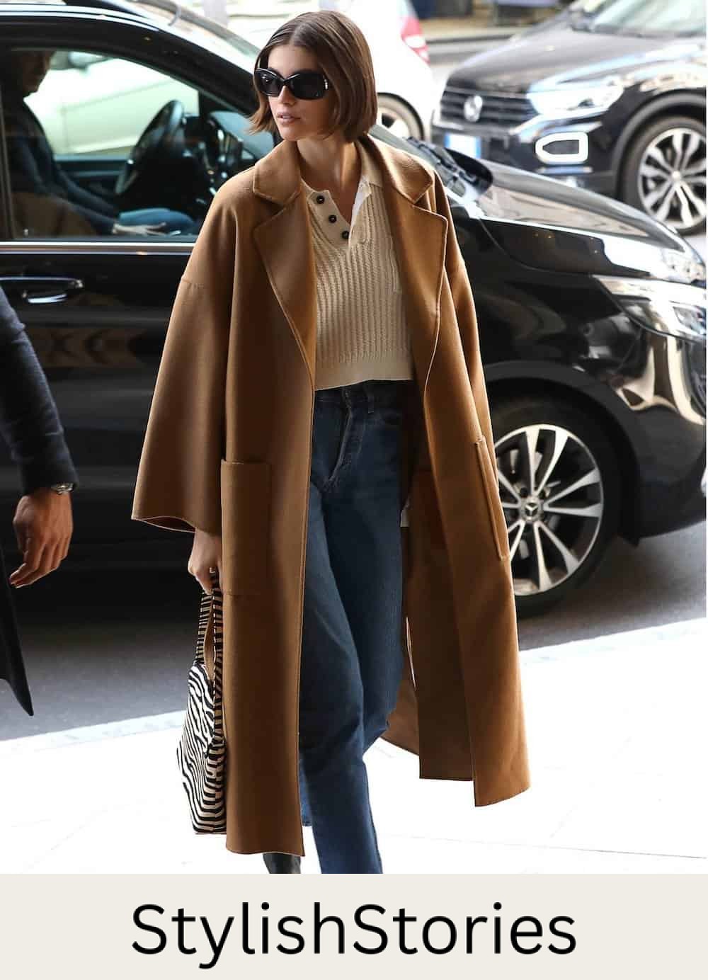 Off-duty model Kaia Gerber wearing jeans, a cropped sweater and a camel colored trench coat.