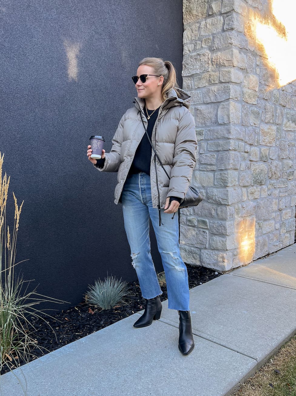 woman wearing a taupe puffer jacket that is an Artizia Super Puff jacket dupe over a black sweater with blue jeans and black ankle boots