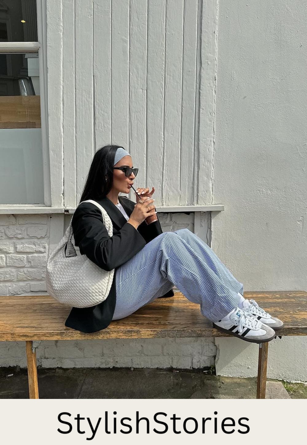 Woman wearing blue and white striped linen pants with a black blazer and white sneakers.