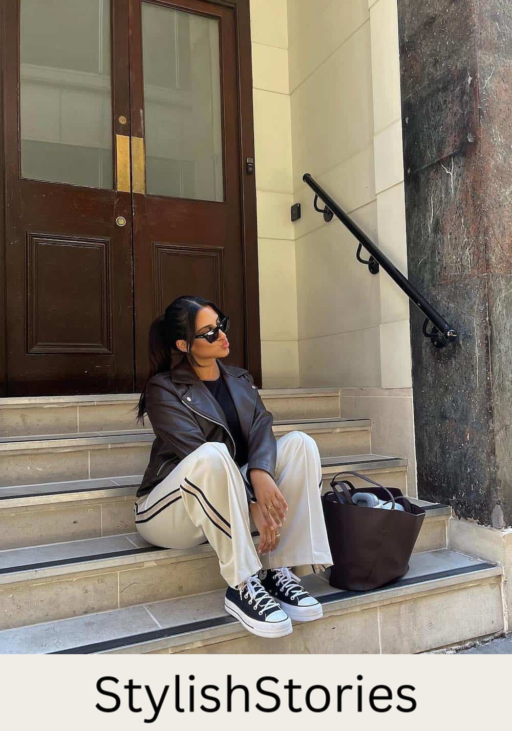 Woman wearing sweatpants with a navy stripe down the side with Converse sneakers and a black leather jacket.