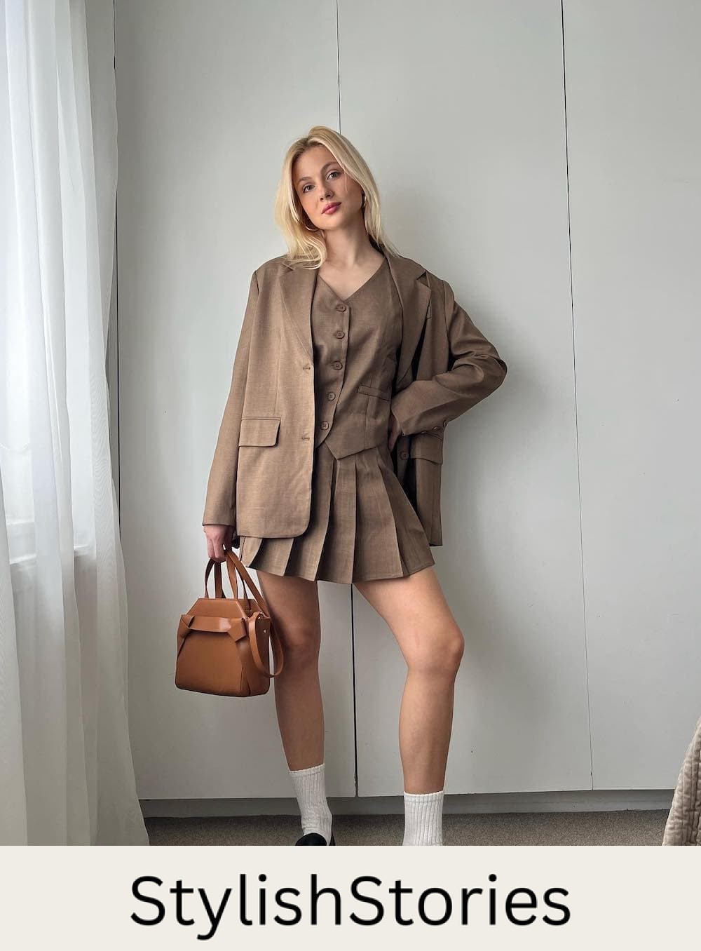 Woman wearing a brown pleated vest and skirt set with a matching blazer and black loafers with tall socks.