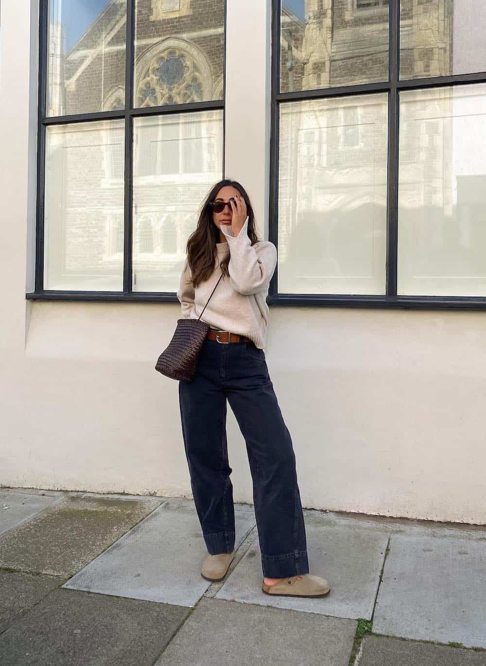 Woman wearing baggy jeans, Birkenstocks and a cream sweater.