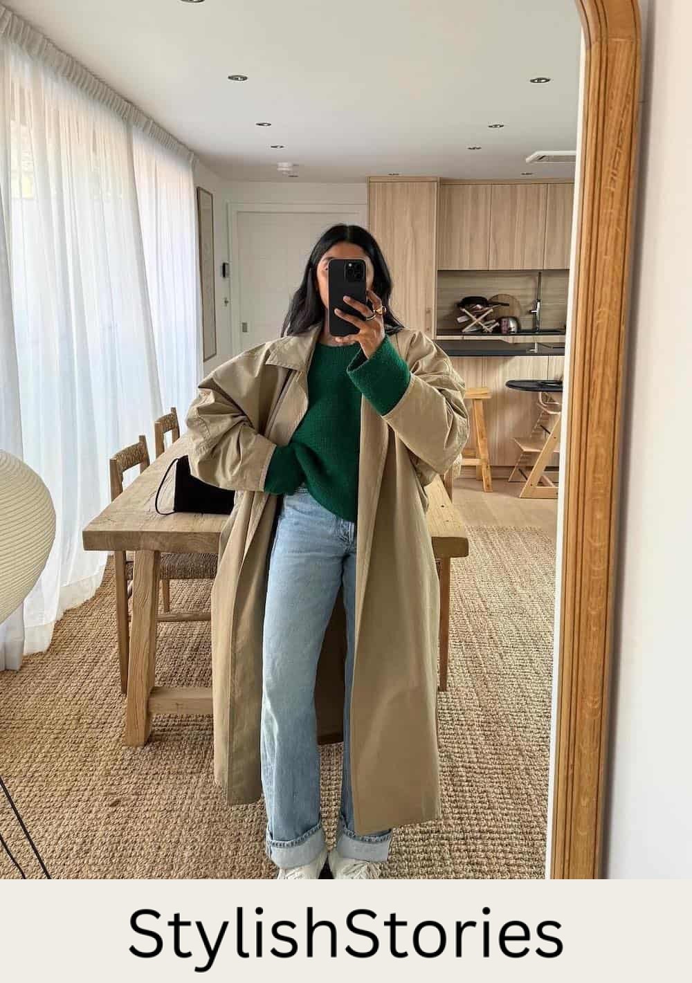 Woman wearing baggy jeans, a green sweater and an oversized trench coat with sneakers.