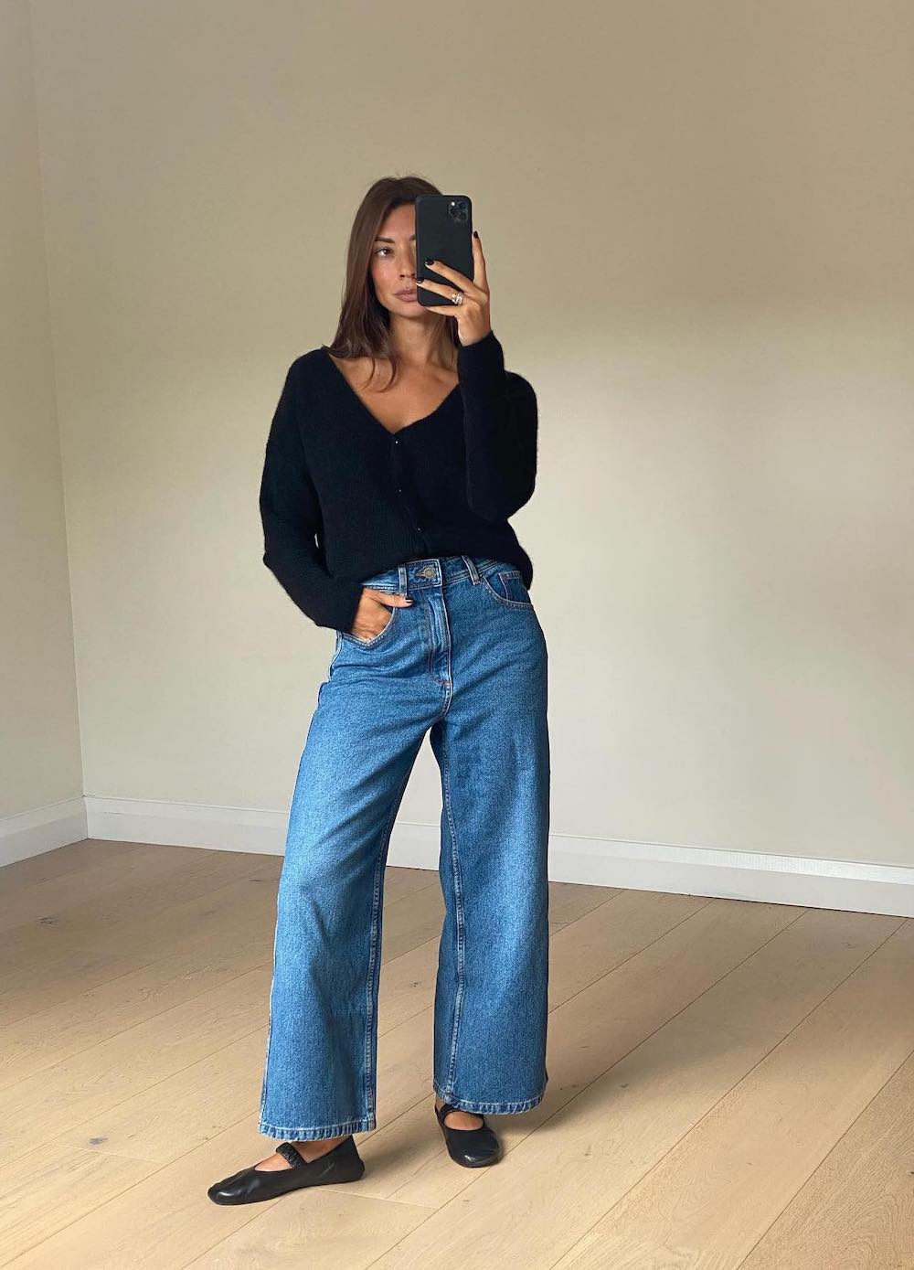 Woman wearing wide leg jeans with black ballet flats and a black cardigan.