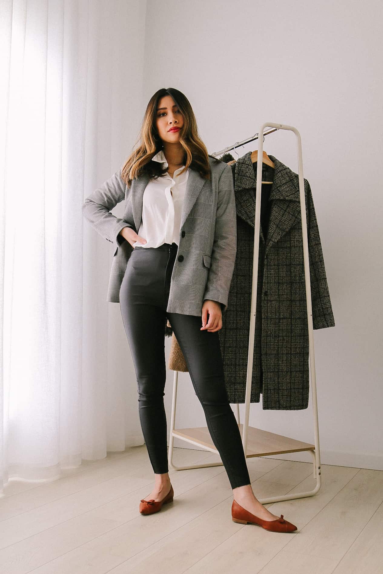 image of a woman wearing a white top, plaid blazer, black leather leggings, and rust colored flats