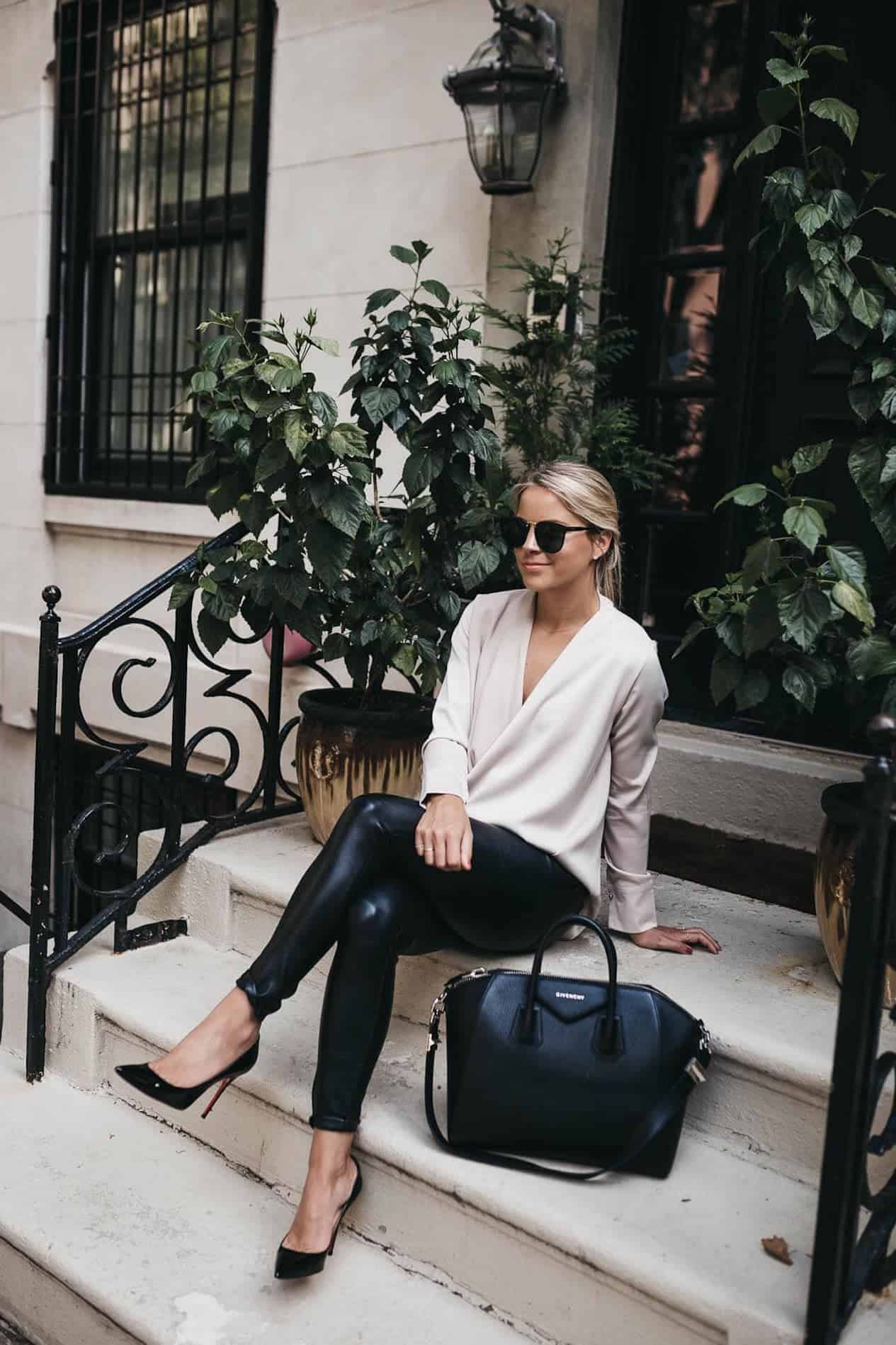 image of a woman sitting on a set of steps wearing a white blouse, black leather leggings, and black pumps