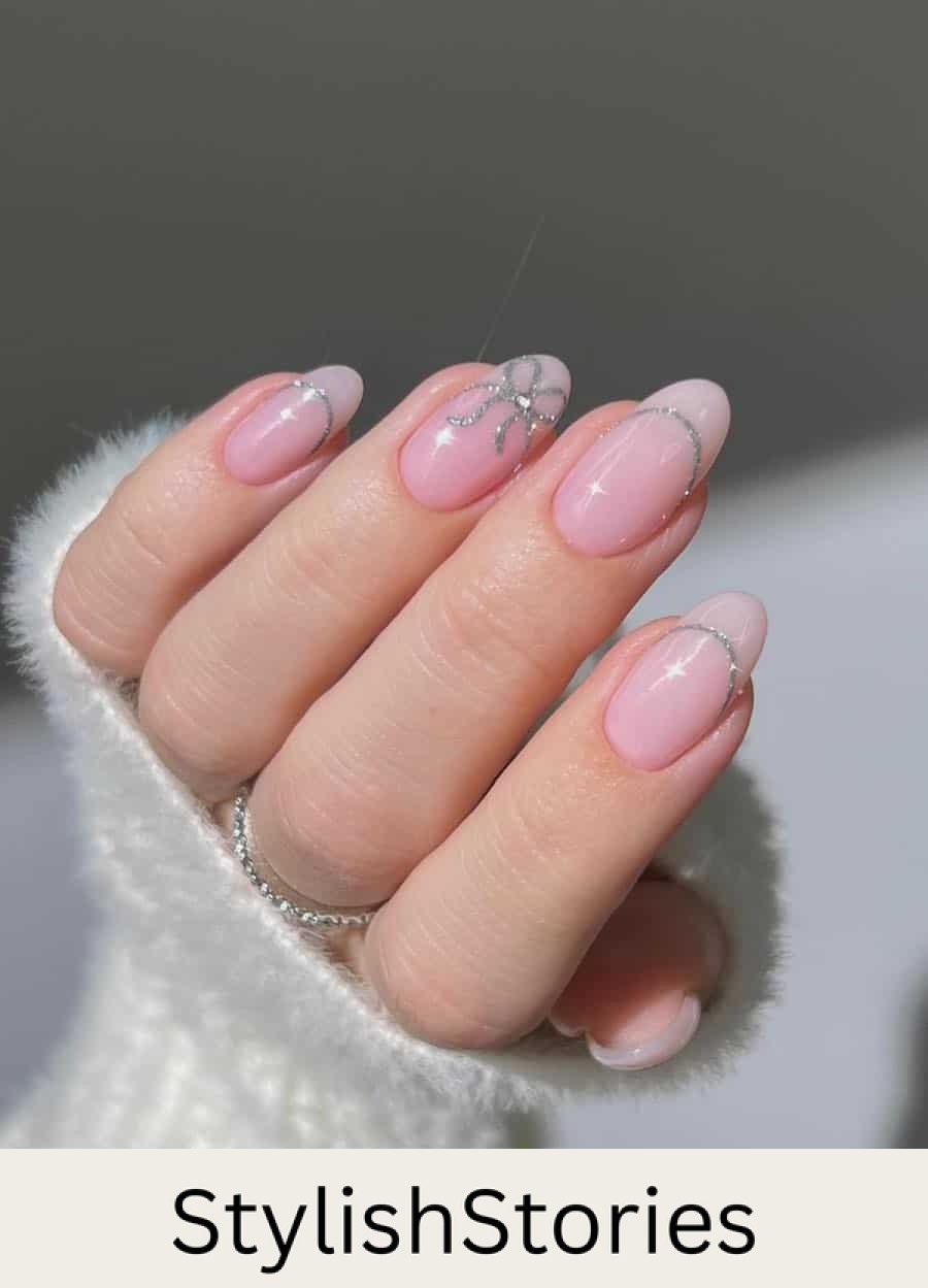 Medium round nails painted a glossy light pink with silver glitter French tip outlined and a bow accent nail