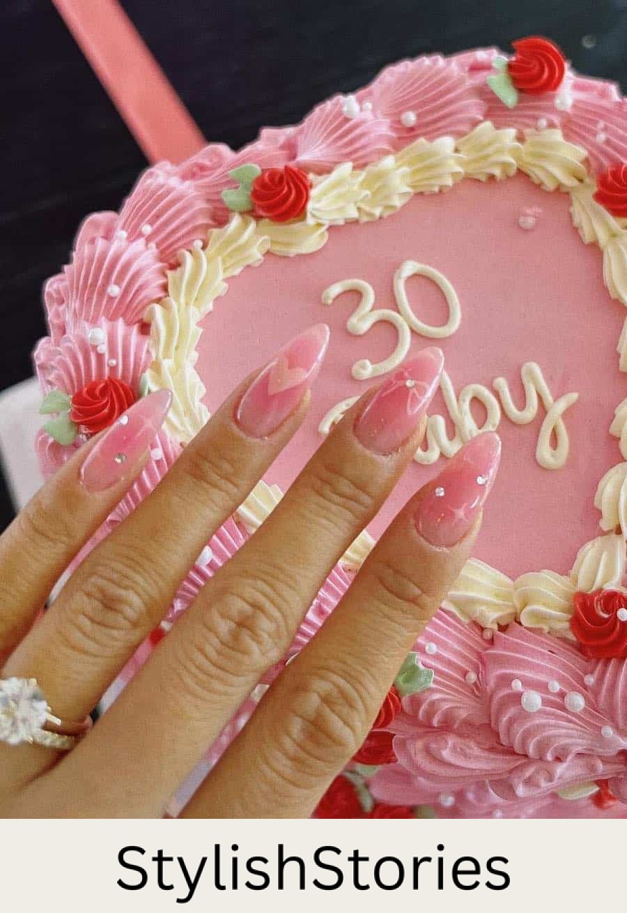 Long almond nails with jelly pink polish and coquette details like hearts, bows, sparkles, and crystals