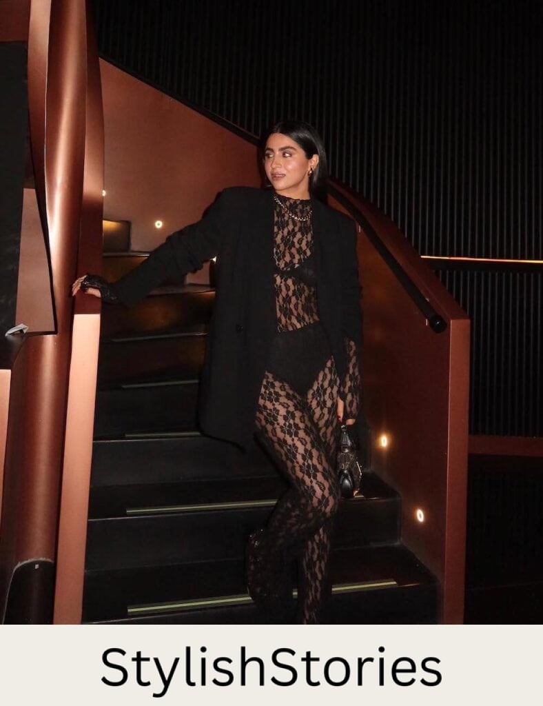 woman wearing a long see through black lace jumpsuit with black undergarments and a black oversized blazer