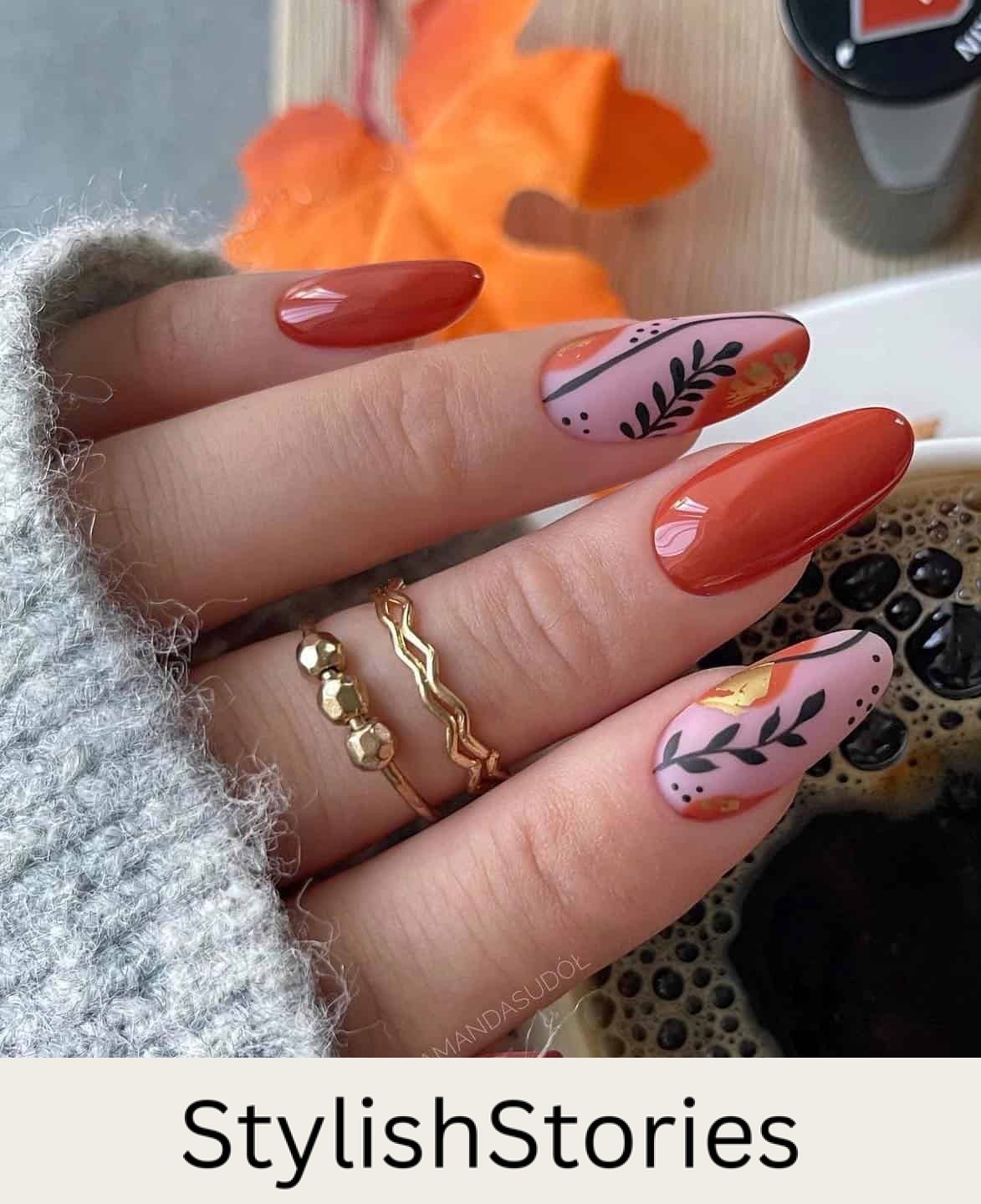 a hand with long almond nails painted in glossy burnt orange and matte pink with black botanical art and gold details