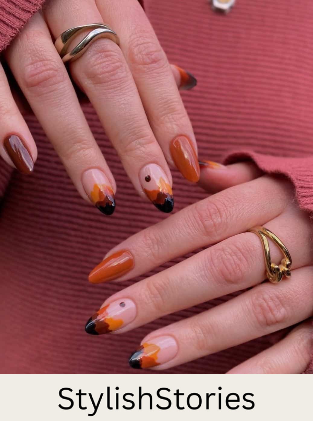 a hand with medium length almond nails painted in solid-colored brown and burnt orange with accent nails featuring mountain inspired nail art