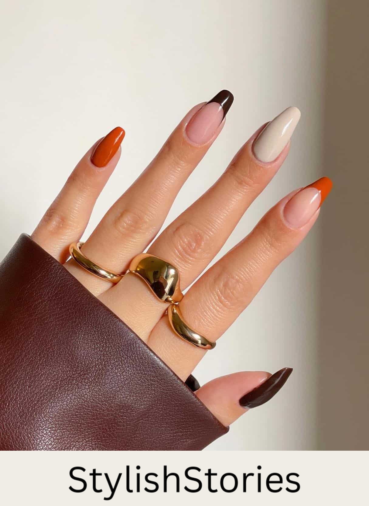 A hand with burnt orange, dark brown, and cream solid-colored nails plus two accent nails with French tips