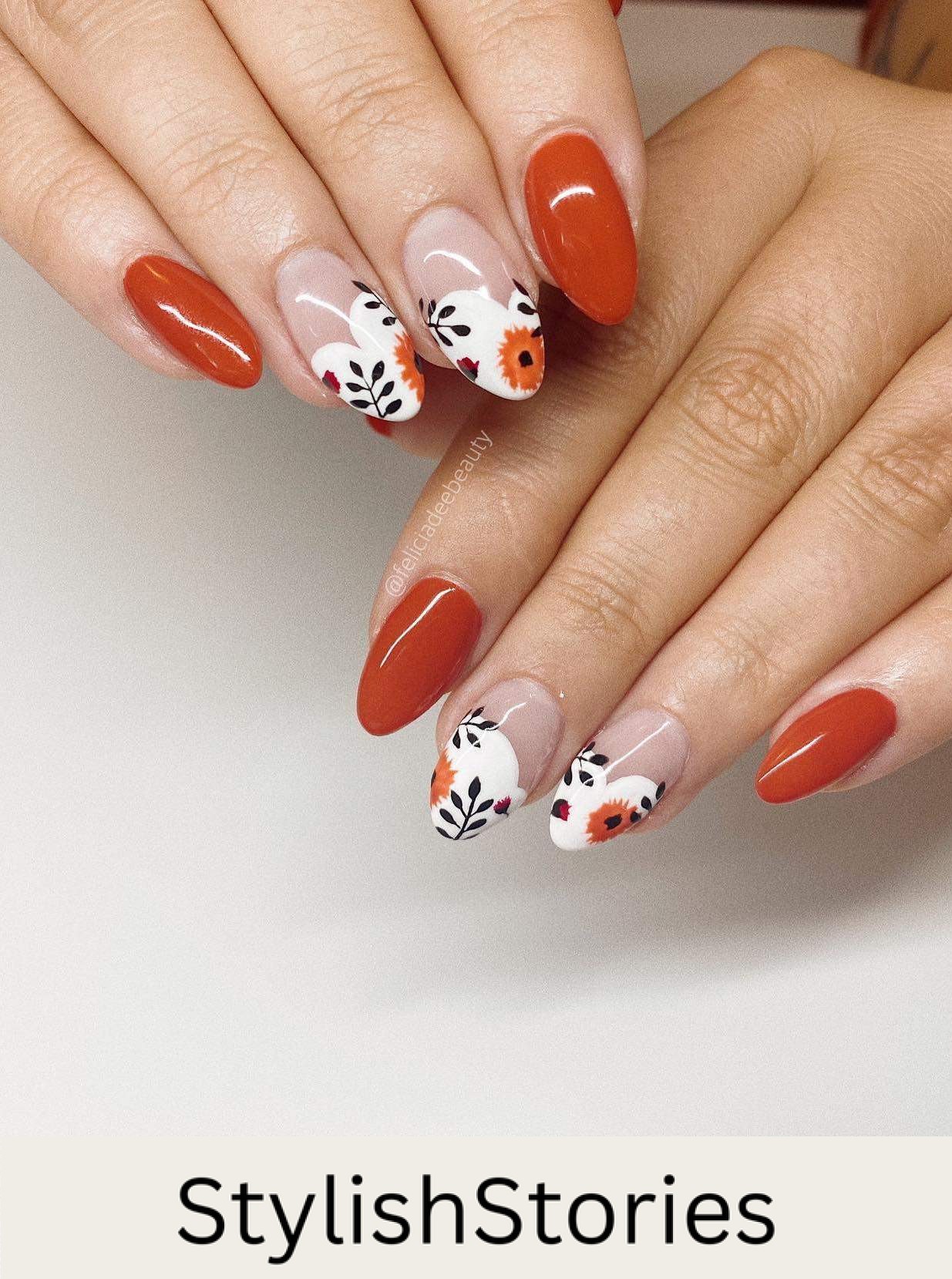 a hand with medium almond nails painted in solid-colored burnt orange and white French tipped accent nails with floral nail art