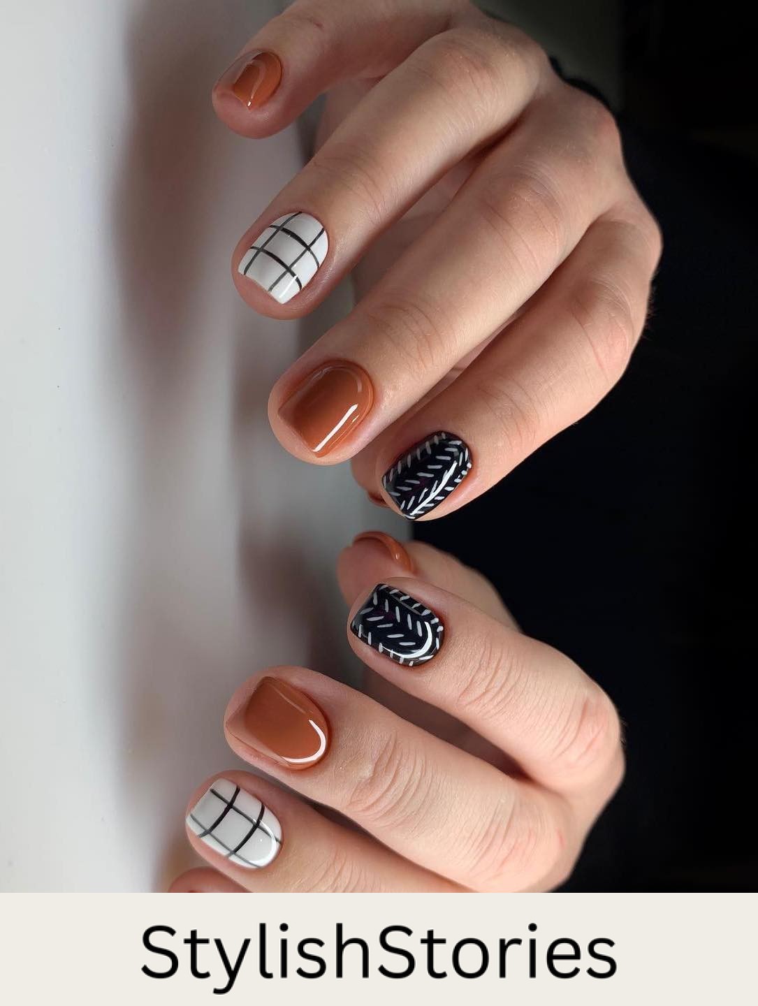 a hand with short square nails painted with solid colored burnt orange, white nails with black grids, and black nails with a white line pattern