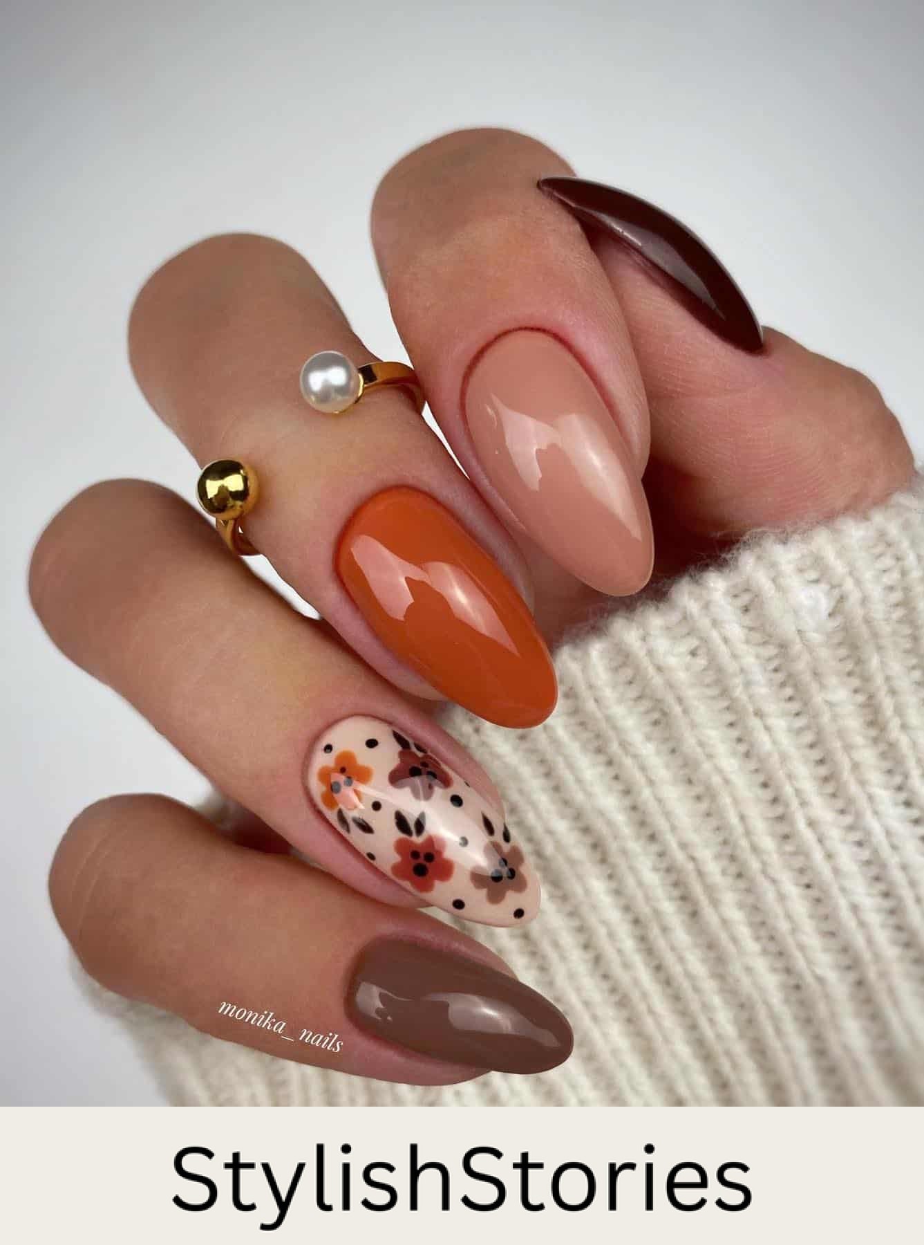 a hand with burnt orange, beige, and brown solid-colored nails plus one cream accent nail with floral art