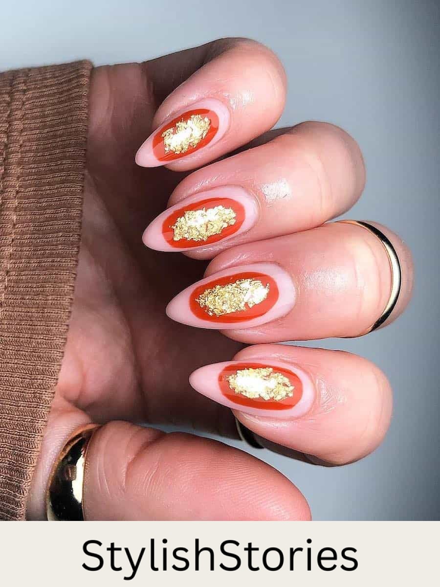 a hand with medium-length almond nails painted a nude pink and burnt orange ovals with gold flakes in the center