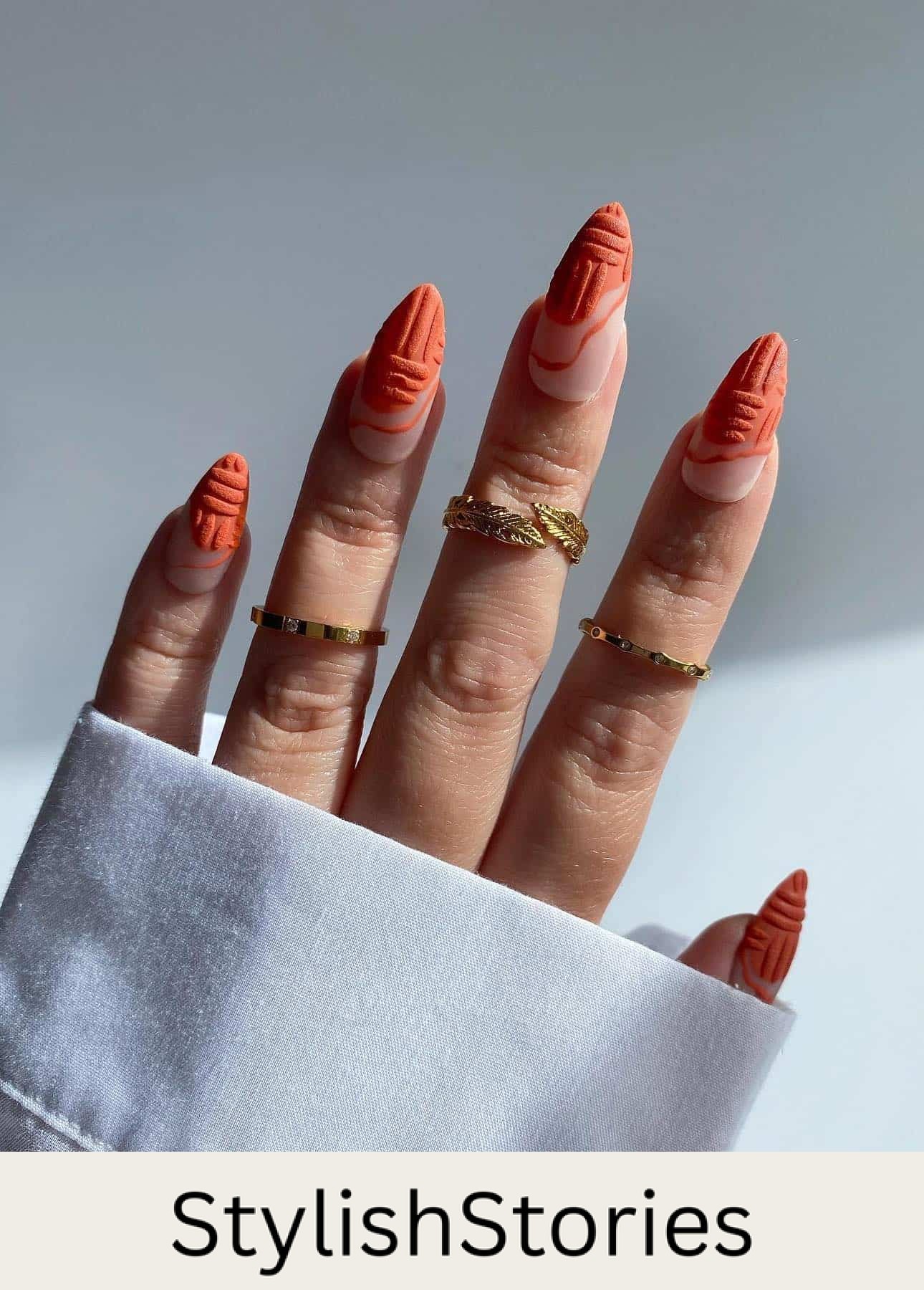 a hand with long stiletto nails painted a nude base with textured, wavy matte burnt orange French tips