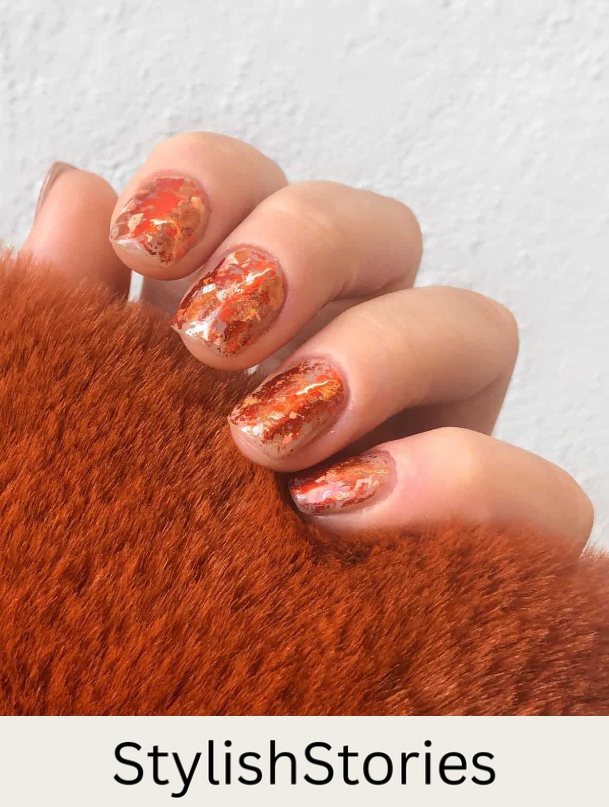 a hand with short square nude nails with burnt orange metallic flakes