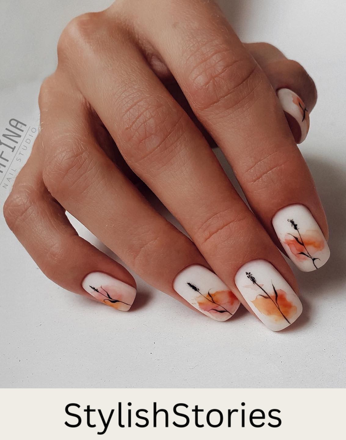 a hand with short white nails featuring an abstract burnt orange splotch and black floral art