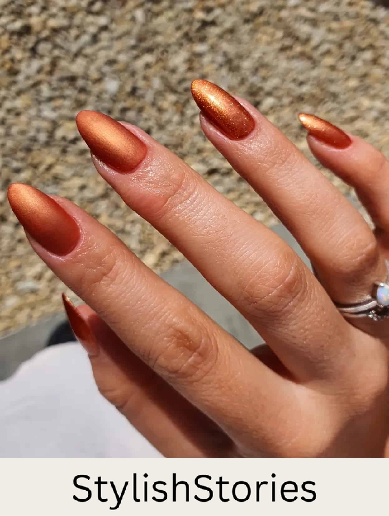 a hand with medium length nails painted burnt orange with a shimmering finish