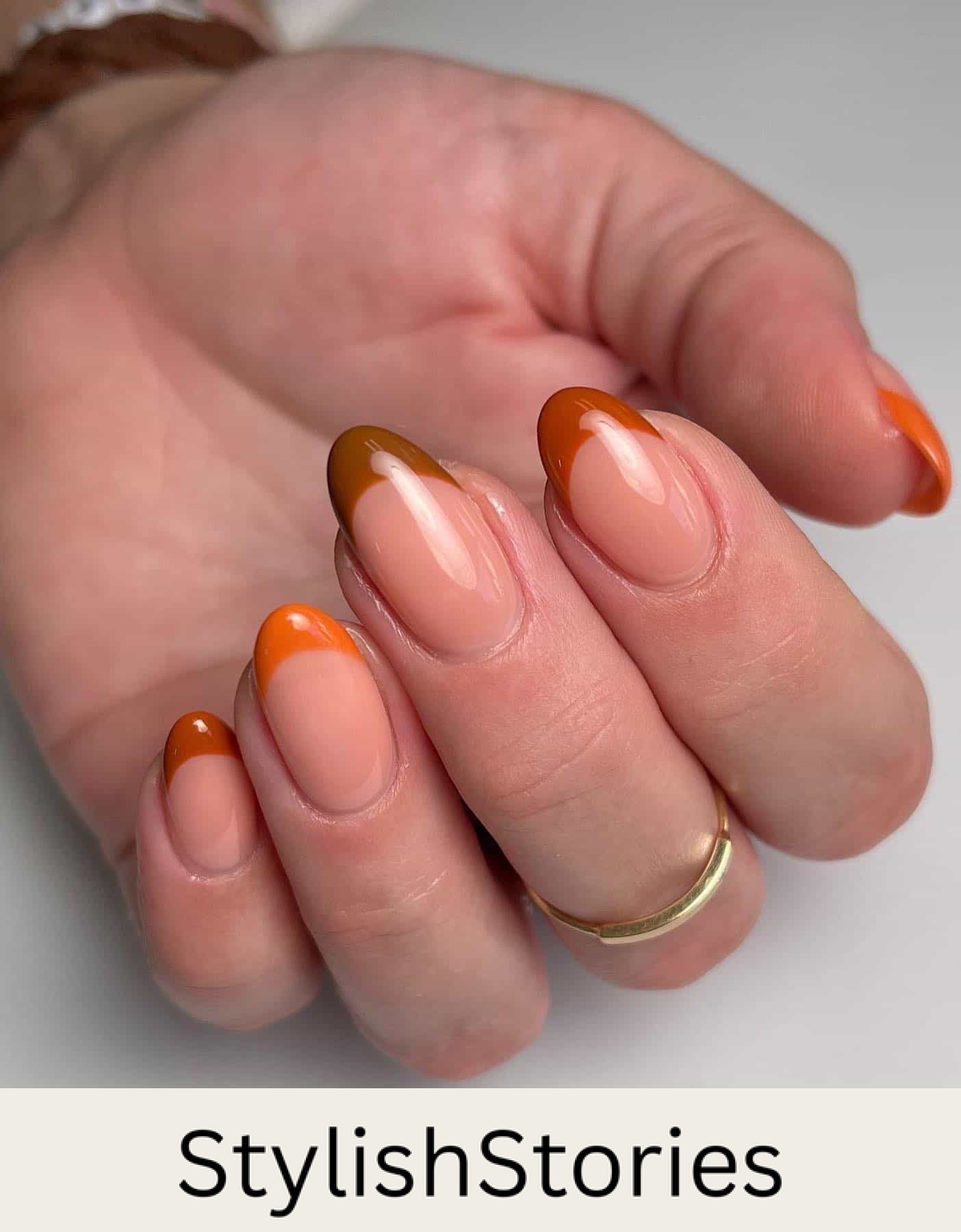 a hand with short round nails painted a glossy nude base with gradient brown, orange, and burnt orange French tips