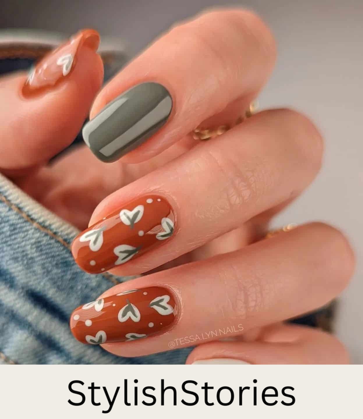 a hand with medium squoval nails painted a burnt orange with leaf nail art and two solid-colored accent nails in white and dark green