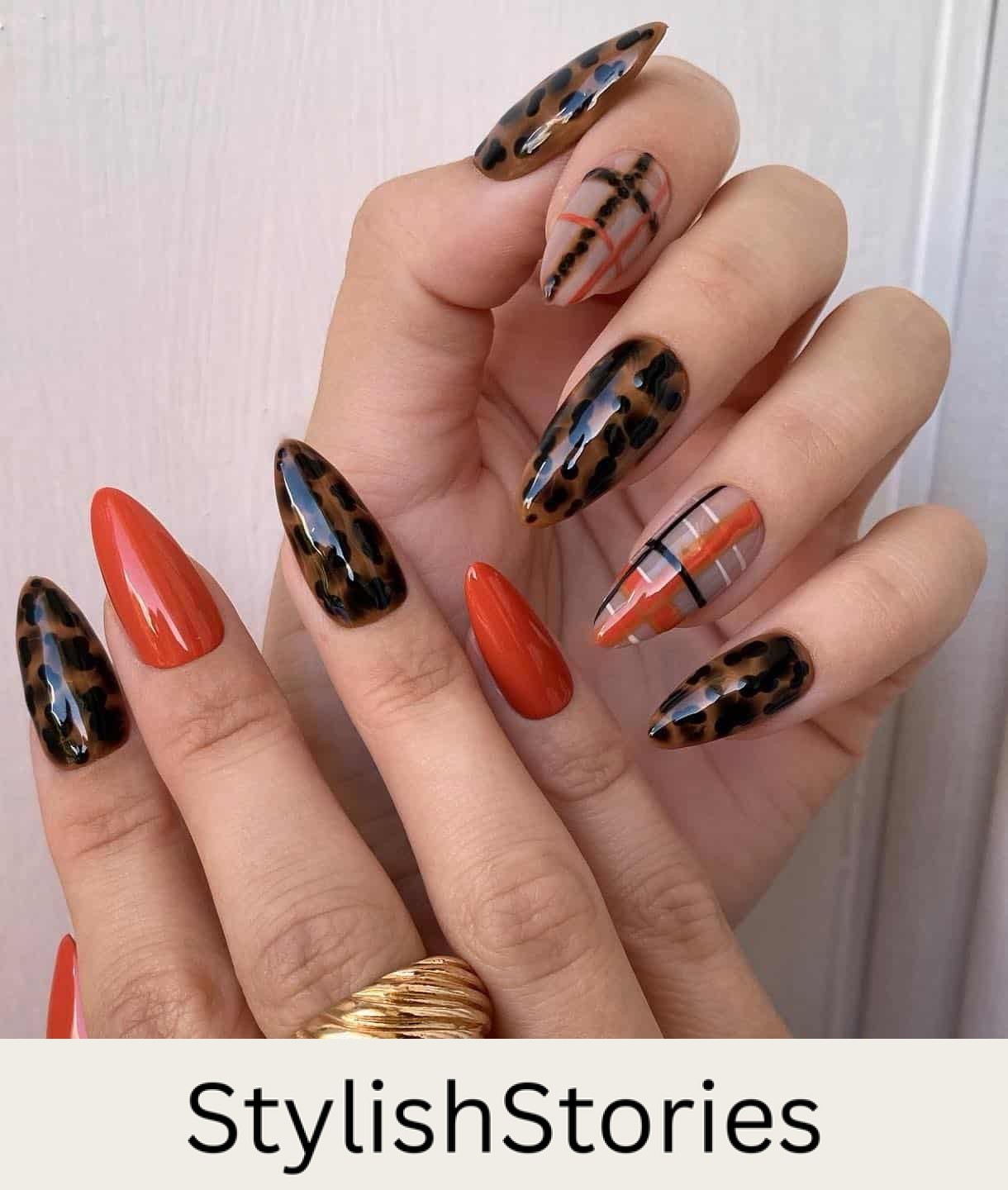a hand with medium stiletto nails featuring multiple designs including solid colored burnt orange nails, black and brown tortoise shell nails, and black, white, and orange plaid nails